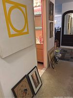 Framed abstract geometric canvas artwork and various framed pictures leaning against a wall in hallway