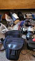 Overview of the lot showing various cameras, lenses, camera cases, and accessories placed on carpeted floor.