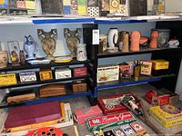 Shelf view showing ceramic fish statue, large ceramic vases with pear motif, handcuffs boxes, and assorted boxes and games below