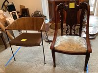 Pair of chairs on carpeted floor, showing mid-century metal chair with rope wrapped back and carved wood chair with patterned upholstery and decorative backrest.