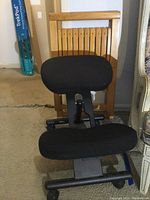 Front view of the kneeling chair positioned in front of the wooden folding chair.