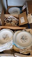 Boxed set of fine china plates and wrapped cups with visible floral pattern and gold rim