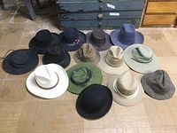 Overview of 14 assorted men's hats laid out on floor, including cowboy, sun, and casual hats in various colors and materials.