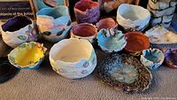 Photo showing thirteen handmade pottery pieces including bowls and vases of various colors and textures on carpet
