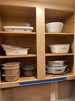 Cabinet shelves displaying multiple Pyrex, Corningware and Anchor Hocking casserole dishes and bowls with lids and patterns visible.