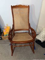 Front view of caned wooden rocking chair showing woven cane seat and backrest, curved armrests, and turned legs.