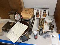 Overview of lot including two mechanical scales, wooden box, brass weights, paint bottles, and small miscellaneous items arranged on a table surface