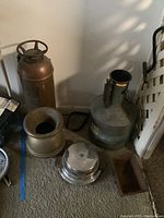 Photo showing the vintage decorative brass fire extinguisher, brass spittoon, metal planter, waffle iron, and galvanized drum marked Seraphin on carpeted floor.