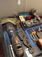 View of carved wooden wall hangings including a mask and decorative panel, alongside woven tapestry textiles and other small accessories.