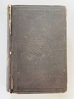 Front cover of the book in black cloth with embossed emblem, shows general condition and wear to edges.