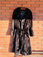 Front view of dark brown mink fur coat on wooden hanger against brick background