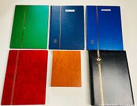 Overview of six Unitrade brand stamp albums in various colors arranged on a white surface.