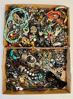 Overhead view of two cardboard trays filled with assorted vintage jewelry including bracelets, necklaces, rings and earrings.
