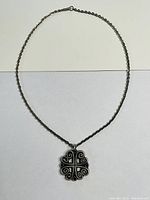 Photo of full necklace laid flat showing chain and pendant with symmetrical four-lobed pewter pendant featuring black enamel cross and swirls.