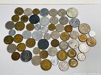 Top-down photo showing an assortment of 60+ old coins arranged on a white background, displaying various sizes, metals, and designs.