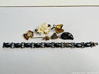 Top view of all jewelry items laid out including bracelet, pins, locket and brooch for identification and condition assessment.