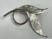 Front view of two leaf silver brooch with detailed engraved pattern and circular element, showing overall shape and design.