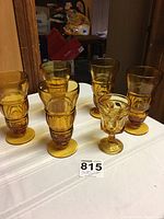 Front view of 5 amber sundae glasses and 1 amber water glass on a white surface with background items.