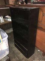 Front view of the black wooden bookshelf showing three shelves and two bottom drawers.