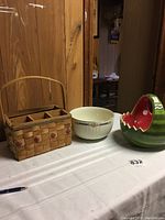 Photo of the three items on a white tablecloth: a woven basket with handle, white Hall Superior floral bowl, and watermelon-shaped bowl