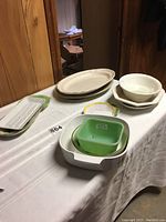 Photo displaying the various bowls and platters on a white tablecloth with wood-paneled wall background, showing shapes and arrangement