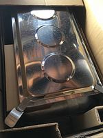 Photo showing the stainless steel chafer lid with three circular depressions and side handles, inside the box.
