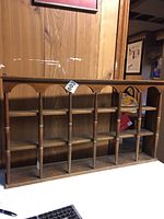 Front view of the wall-mounted wooden display rack showing multiple compartments for cups and saucers against a wood paneled wall.