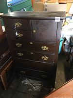 Front view of dark wood dresser showing multiple drawers and small door, with some missing handles