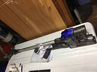 Full view of Dyson DC35 handheld vacuum cleaner lying on a white table showing the main unit, wand, and wand-mounted cleaning head.