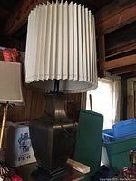 Large lamp with beige pleated shade and dark brass square base, placed on wood surface.