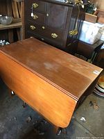 View of the closed maple drop leaf table showing the top surface and side leaves, placed indoors among other furniture.