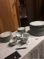 Full view of stacked dinner plates, sandwich plates, saucers and cups on a table, showing the Mikasa Margaret china pattern with delicate floral and gold scroll designs and silver edges.