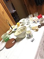 Overview of kitchen items on table showcasing bowls, mugs, glasses, small tools, and other kitchenware arranged with some labels visible