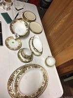 Partial Noritake No. 175 set displayed on table showing platters, bowls, gravy boat, cups and saucers with gold ornate design, Lenox and Flintridge plates.