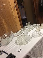 Photo of the lot showing the platter, frosted bowl, oval dish, Waterford creamer, Mikasa candle holders, nappy, votives, bell, and Mikasa clock arranged on a white tablecloth.