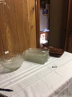 Punch bowl and luncheon trays displayed on table with white cloth, items clearly visible including clear pressed glass bowl and trays with raised patterns and brown trays.