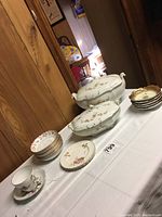 Side view of Johnson Bros. tureens and stacks of plates and saucers on white tablecloth.