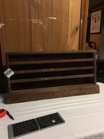 Photo showing entire wooden display shelf unit placed on a white surface in front of a wooden cabinet for size context.