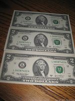 Three US two dollar bills laid flat showing front side with Thomas Jefferson portrait and sequential serial numbers.