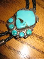 Close-up of the bolo tie centerpiece showing large turquoise stone and smaller turquoise accents in silver-tone setting.
