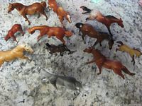 Top-down view of 11 Breyer horse and colt figurines in various colors and poses on a speckled surface.