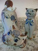 Two handmade ceramic cat figurines detailed with floral patterns in traditional Mexican style, one with damaged ear