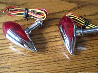Two chrome bullet marker lights with red top lens, wiring attached, placed on a wooden surface.