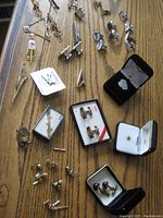 Wide view of men's cuff links, pins, and tie bars spread out on a wooden surface, some in original boxes.