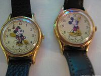 Close up of two Mickey Mouse wristwatches showing watch faces with Mickey pointing to time and gold-tone cases