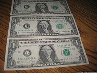 Three unfolded and crisp one dollar bills from 1981 laid flat on a wooden surface, front side visible showing George Washington portrait and green treasury seal.