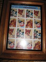 Framed sheet of Disney postage stamps shown flat with clear view of all stamps and wooden frame