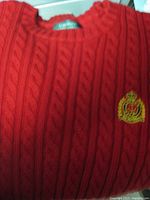 Close-up of red cable knit design and embroidered Ralph Lauren logo crest on left chest, showing knit pattern and sweater neckline.