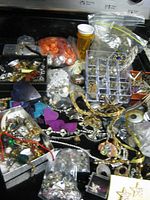 Photo depicting a large assortment of jewelry scrap items including beads, charms, chains, and pendants in various colors and materials scattered on a surface.