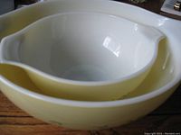 Two nested Pyrex mixing bowls, floral design, white inside, yellow outside, larger bowl 13 inches wide